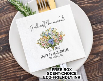 May include: White square napkin with the text "Fresh off the market" and a floral bouquet design. The napkin also includes "EST. 2026", "EMILY'S BACHELORETTE", and "LOS ANGELES, CA". The napkin is on a white plate with a fork and knife.