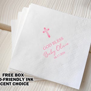 May include: White paper napkins with a pink cross, the text "God Bless Baby Olivia 08.17.2026" and a decorative border.