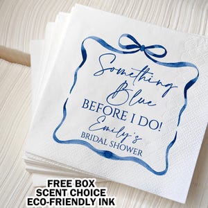 May include: White paper napkins with a blue ribbon design and the text "Something Blue BEFORE I DO! Emily's BRIDAL SHOWER". The napkins are stacked, and the text is in a script font.