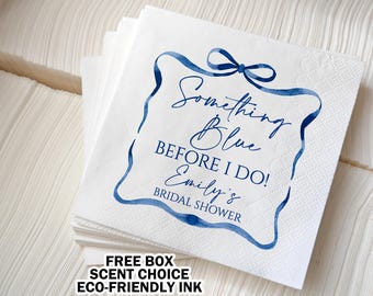 May include: White paper napkins with a blue ribbon design and the text "Something Blue BEFORE I DO! Emily's BRIDAL SHOWER". The napkins are stacked, and the text is in a script font.