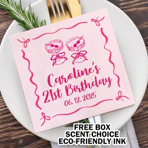 May include: Pink paper napkin with a pink border and a design of two cake pops. The text reads "Caroline's 21st Birthday 06.12.2025".