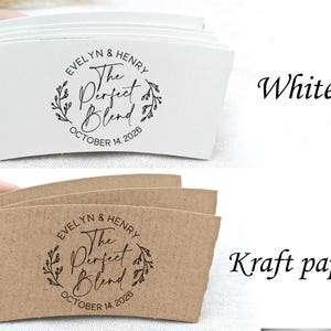 May include: White and kraft paper coffee cup sleeves with the text "EVELYN & HENRY The Perfect Blend OCTOBER 14, 2026" printed in black. The design includes a floral wreath. The sleeves are shown in a stack.
