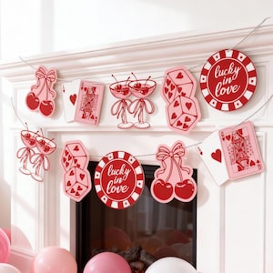 May include: A decorative banner with a Valentine's Day theme. The banner features cutouts of cherries, dice, playing cards, and casino chips with the text "lucky in love". The color scheme is red and pink.
