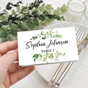 May include: White table card with green watercolor foliage and gold accents. The text reads "Sophia Johnson Table 1".