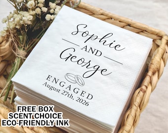 May include: White card stock announcement with black text that reads "Sophie and George Engaged August 27th, 2026". The card is sitting in a wicker basket with a bouquet of white flowers.