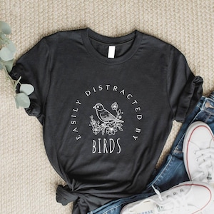 May include: A black t-shirt with a white graphic design that says "Easily Distracted By Birds" with a small bird illustration.