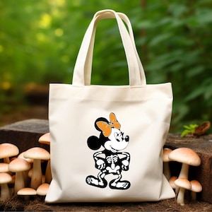 May include: A white canvas tote bag with a black and white image of a skeleton Mickey Mouse character wearing an orange bow. The character is standing with its arms crossed.