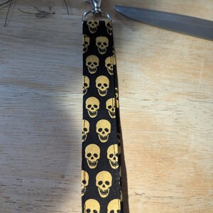 May include: A black and gold lanyard with a skull pattern. The lanyard has a silver metal clip.