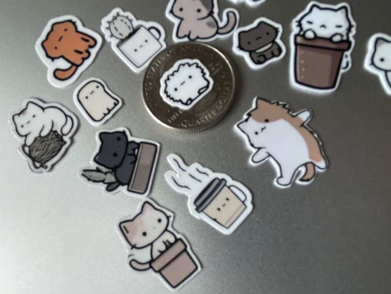 Puede incluir: Una colecci&oacute;n de pegatinas con tem&aacute;tica de gatos, que representan gatos de dibujos animados en varias poses. Las pegatinas muestran gatos en macetas, con hilo y otros dise&ntilde;os l&uacute;dicos. Se incluye una moneda para referencia de tama&ntilde;o. Las pegatinas son coloridas y tienen un acabado brillante.