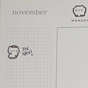 Puede incluir: Una p&aacute;gina de planificador con la palabra "noviembre" en la parte superior. Una pegatina de un animal de dibujos animados con un sombrero de vaquero con las palabras "Yee Haw!" est&aacute; en la cuadr&iacute;cula. Un peque&ntilde;o animal de dibujos animados est&aacute; en la esquina superior derecha con la palabra "lunes" debajo.