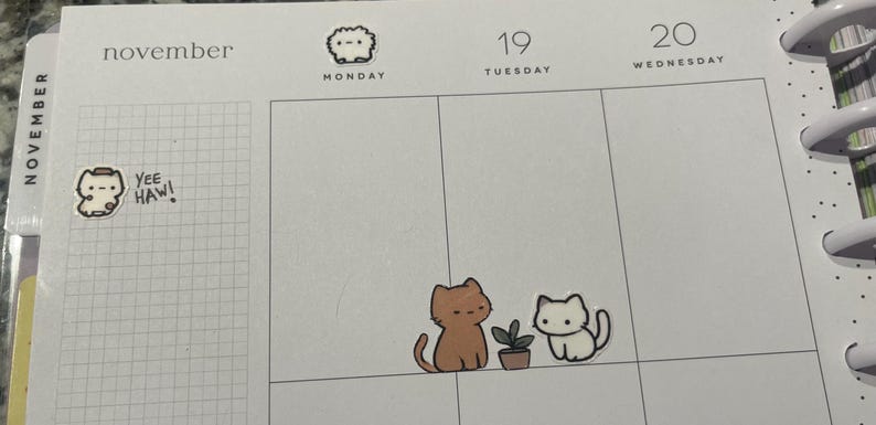 Puede incluir: Una p&aacute;gina de planificador con pegatinas con tem&aacute;tica de gatos. Una pegatina dice "Yee Haw!". Dos pegatinas de gatos est&aacute;n cerca de una peque&ntilde;a planta en maceta. La p&aacute;gina est&aacute; marcada para el 19 y 20 de noviembre.
