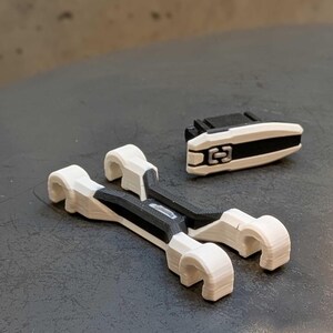 May include: A set of 3D-printed white and black plastic components. Two larger pieces have a curved design with a central black section. A smaller, rectangular piece with a black stripe and a central design is also present.