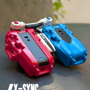 May include: A red and a blue dual launcher link for string launchers. The red launcher has a black top and white accents. The blue launcher has a black top. The text "X-SYNC" and "DUAL LAUNCHER LINK FOR STRING LAUNCHERS" are visible.