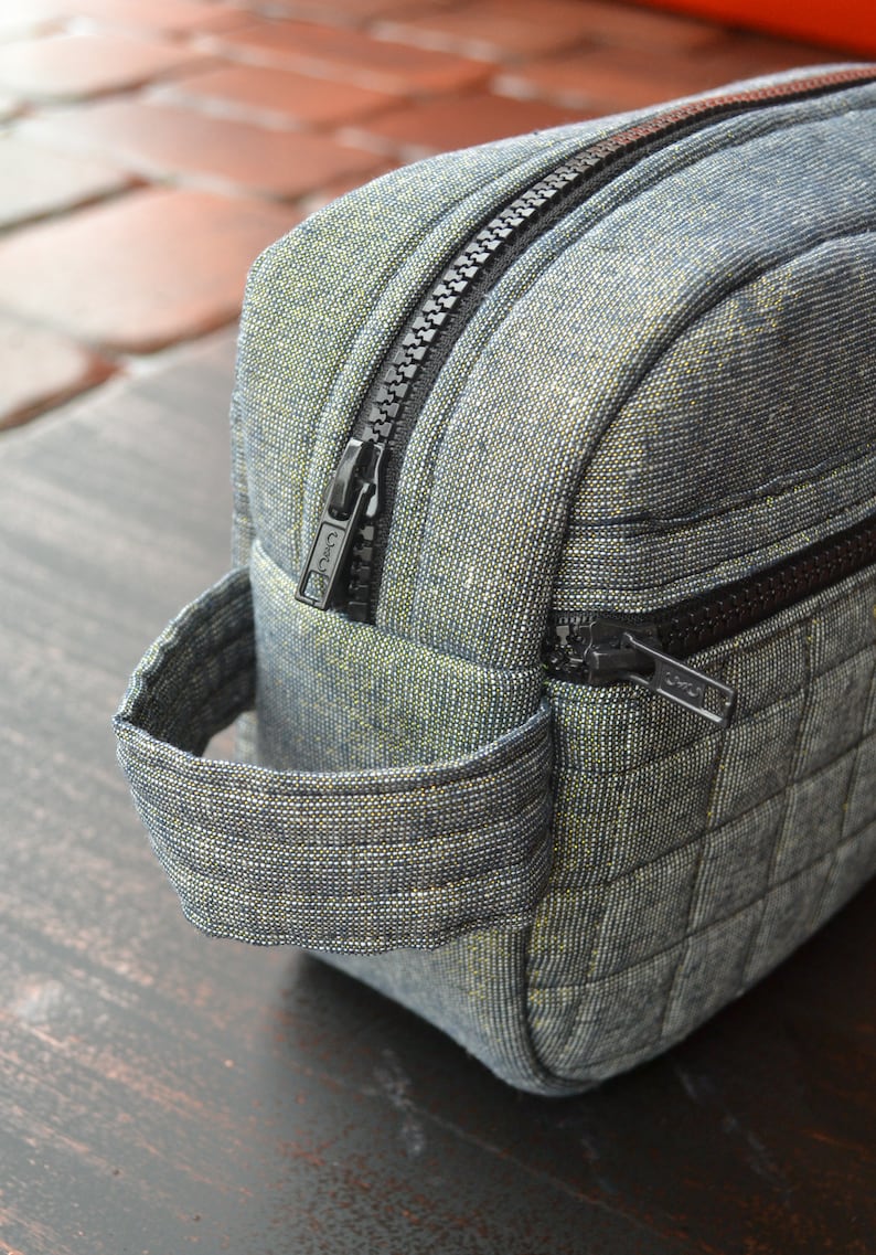 May include: A gray quilted toiletry bag with a black zipper and a black handle. The bag has a small zippered pocket on the side.