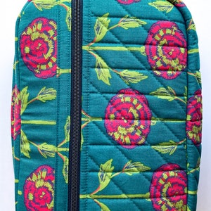 May include: Teal quilted zippered pouch with a floral print featuring pink and green flowers. The pouch has a top handle and a zipper closure.