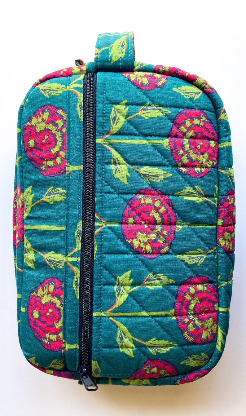 May include: Teal quilted zippered pouch with a floral print featuring pink and green flowers. The pouch has a top handle and a zipper closure.