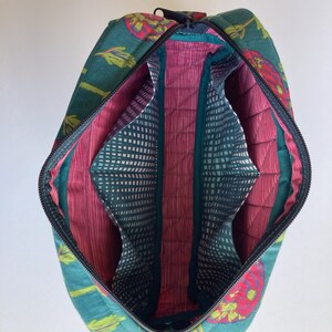 May include: A teal and red floral print zippered travel bag with a pink quilted interior and multiple compartments. The bag has a top handle and a zipper closure.