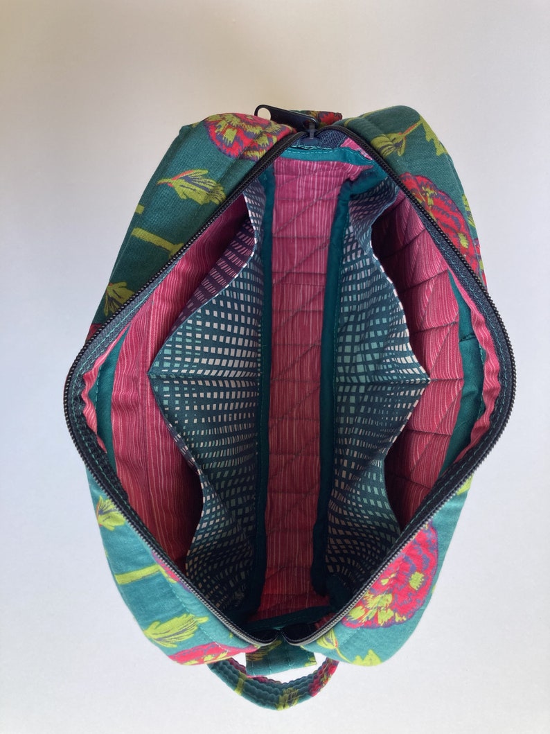 May include: A teal and red floral print zippered travel bag with a pink quilted interior and multiple compartments. The bag has a top handle and a zipper closure.