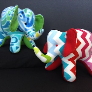 May include: Two plush toy elephants, one with a blue, green and yellow geometric pattern and the other with a red, white and blue chevron pattern.