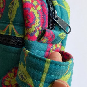 May include: A teal blue zippered pouch with a floral pattern. The pouch has a black zipper and a black strap.