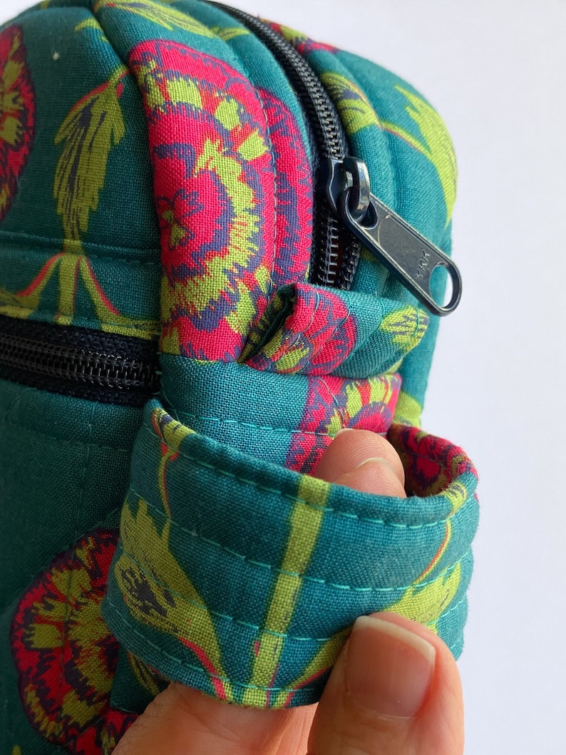 May include: A teal blue zippered pouch with a floral pattern. The pouch has a black zipper and a black strap.