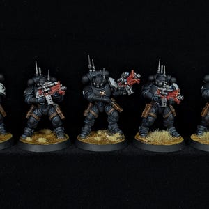Puede incluir: Cinco figuras en miniatura de soldados blindados, cada una sobre una base circular. Las figuras son principalmente negras con detalles rojos y marrones, sosteniendo armas rojas y grises. El fondo es negro.