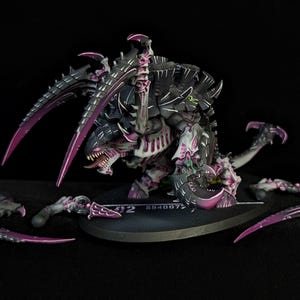 Può includere: Figura in miniatura dettagliata di una creatura Tirannide, con un esoscheletro nero e grigio e vivaci riflessi viola sugli artigli e altre parti del corpo. La figura è posizionata su una base nera, con artigli staccati aggiuntivi nelle vicinanze.