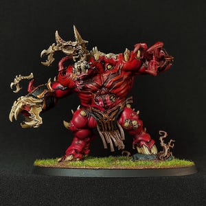 May include: A red and gold painted miniature of a demon with horns, claws, and a fanged mouth. The demon is standing on a circular base with green grass.