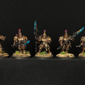 Op de afbeelding: Zes goud geverfde miniatuurfiguren met blauwe en zwarte wapens, staande op ronde bases. De figuren dragen sierlijke harnassen en helmen met rode accenten.