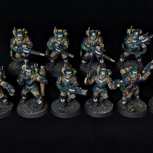 May include: A collection of miniature figurines, each painted with a blue, tan, and green color scheme. The figures are posed with weapons and equipment, standing on textured, circular bases. The overall theme suggests a science fiction or fantasy setting.