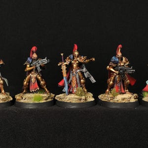 May include: Five miniature figures of female warriors wearing gold armour and red cloaks, holding weapons and standing on circular bases.