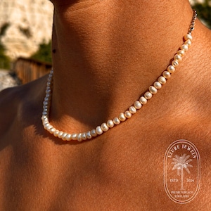 May include: A delicate pearl necklace with a silver clasp. The necklace is composed of small, round, off-white pearls. The image also includes the Azure Jewels logo, ESTD 2024, and Premier Beach Jewellery.