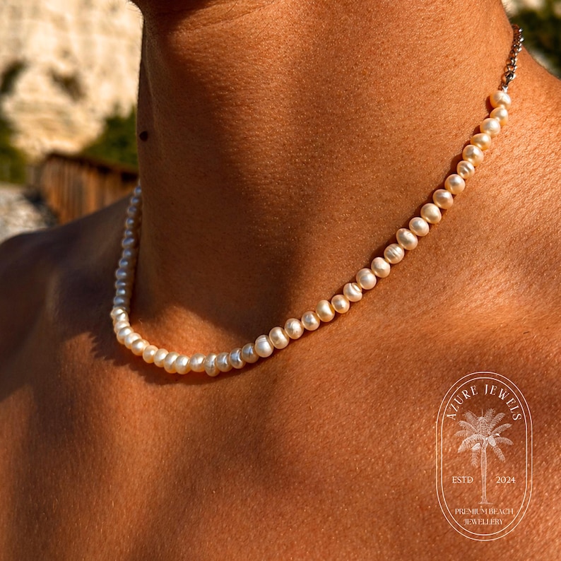 May include: A delicate pearl necklace with a silver clasp. The necklace is composed of small, round, off-white pearls. The image also includes the Azure Jewels logo, ESTD 2024, and Premier Beach Jewellery.