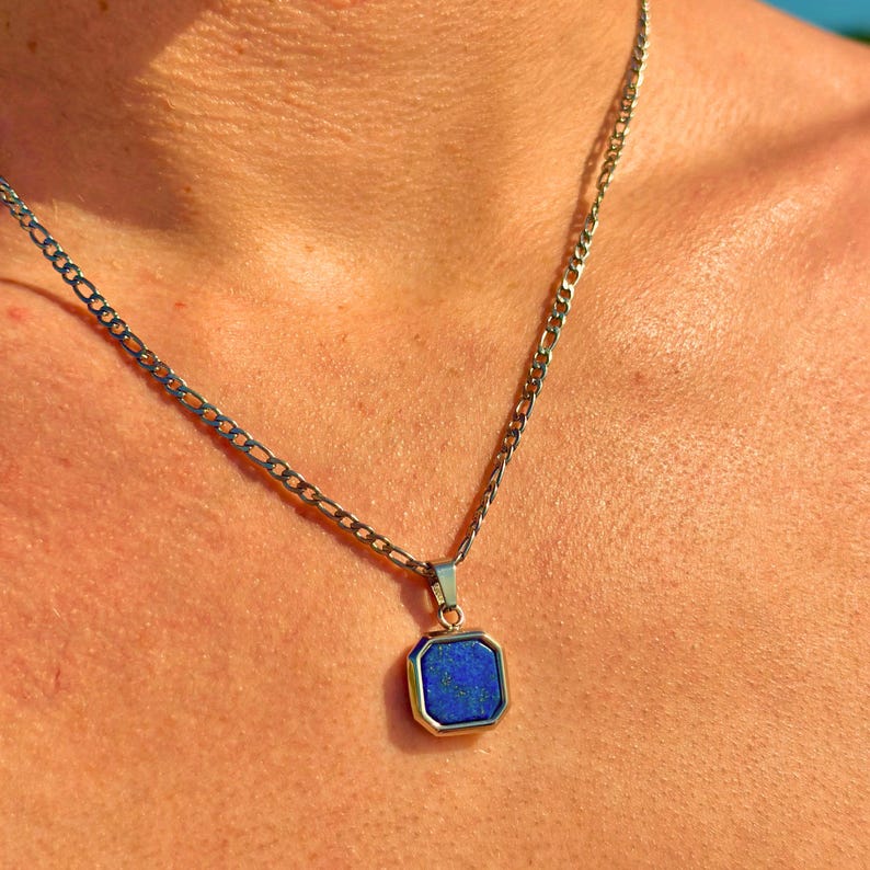 May include: A silver chain necklace with a pendant featuring a dark blue gemstone set in a silver frame.