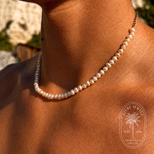 May include: A delicate pearl necklace with a silver clasp. The necklace is composed of small, round, off-white pearls. The necklace is a jewelry item.