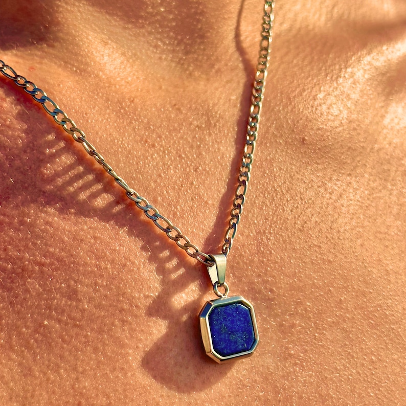 May include: A silver chain necklace with a square pendant featuring a dark blue gemstone.