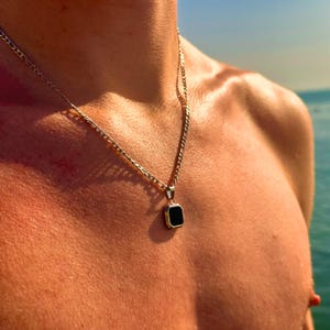 May include: A silver chain necklace with a black square pendant.