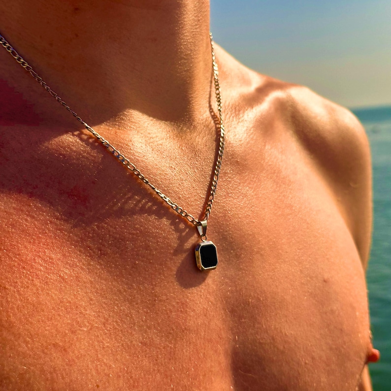 May include: A silver chain necklace with a black square pendant.