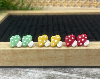 May include: Six small mushroom-shaped earrings in three colors: green, yellow, and red. Each mushroom has white polka dots and a white stem.