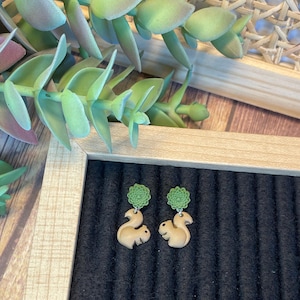 May include: A pair of brown squirrel earrings with green leaves. The earrings are made of polymer clay and are a cute and whimsical accessory.