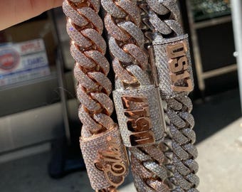 May include: Three gold chains with diamond accents. The chains are layered on top of each other. The chains have different lengths and are adorned with the words "Cole", "1617", and "UST17".