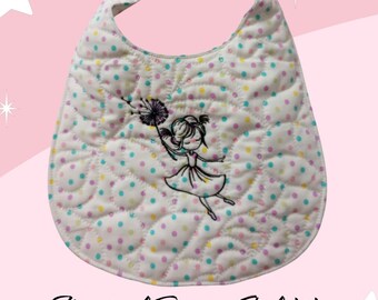 May include: A white quilted baby bib with a colorful polka dot pattern. The bib features an embroidered design of a girl with a flower. The text "Magical Breezy Girl bib 2 snap adjustment." is printed below the bib.