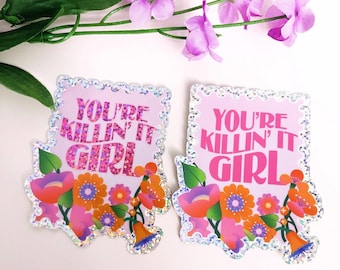 May include: Two stickers with the text "YOU'RE KILLIN' IT GIRL" in pink and purple, surrounded by a floral design with orange, pink, and blue flowers. The stickers have a glittery border and are set against a white background with purple flowers.