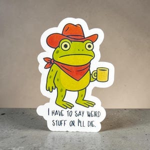 May include: A die-cut sticker featuring a green frog wearing an orange cowboy hat and a red bandana around its neck. The frog holds a yellow mug in one hand. Below the frog, the text reads: I HAVE TO SAY WEIRD STUFF OR I'LL DIE.