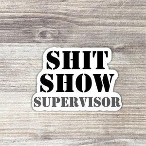 May include: White sticker with black text that reads "SHIT SHOW SUPERVISOR" on a woodgrain background.