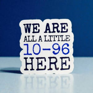 May include: A white die-cut sticker with a wavy edge featuring the text WE ARE ALL A LITTLE 10-96 HERE. The words WE ARE ALL A LITTLE and HERE are printed in dark navy blue, while the numbers 10-96 are printed in a bright royal blue color.