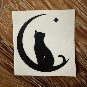 May include: Black silhouette of a cat sitting on a crescent moon with a star above it. The design is on a white background.