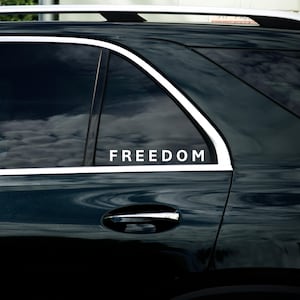 May include: A dark green car window displaying the word "FREEDOM" in white. The window reflects a cloudy sky. The car features a silver roof rack and a chrome door handle.