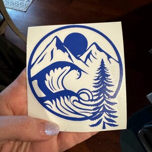 May include: A blue vinyl decal with a mountain range, a sun, a wave, and a pine tree in a circle.
