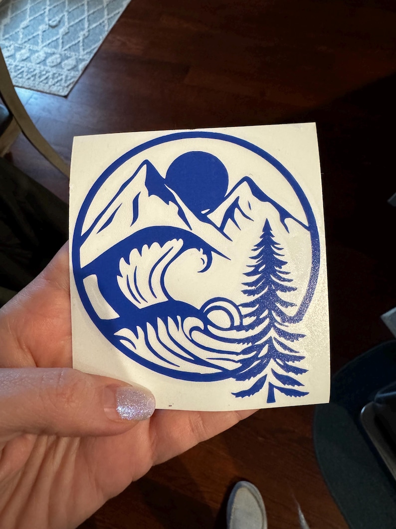 May include: A blue vinyl decal with a mountain range, a sun, a wave, and a pine tree in a circle.